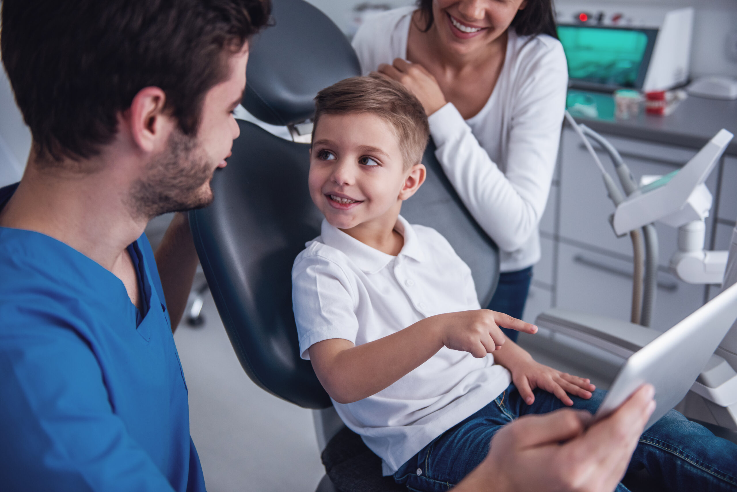 Cute little boy at the dentist. Mom is supporting her son and dentist are using a digital tablet to show digital scans of his teeth