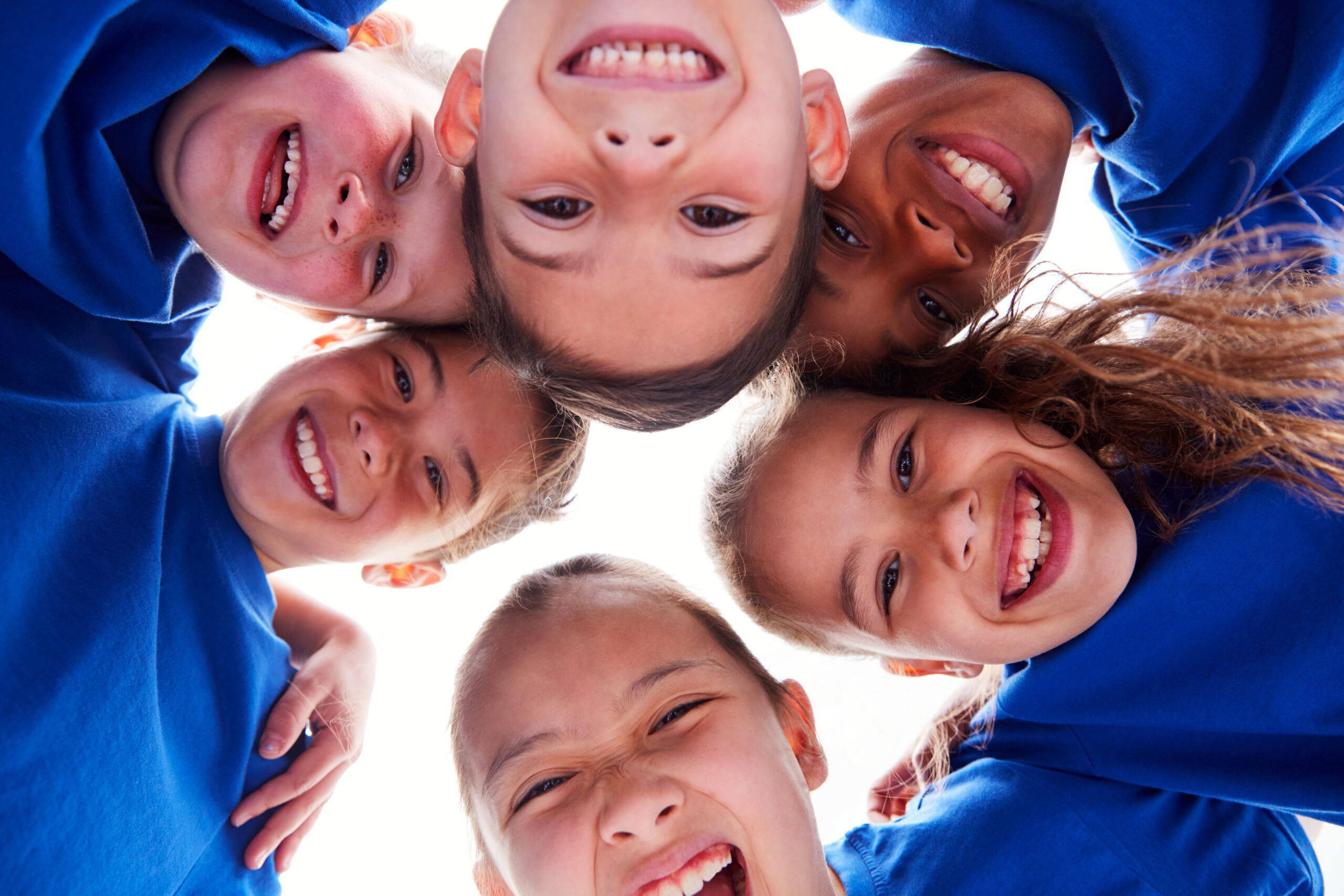 Low Angle View Looking Up Into Faces Of Children In Huddle Smiling