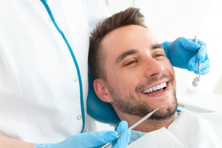 a man is smiling while a dentist examines on his teeth for root canal the dentist is wearing blue gloves and holding