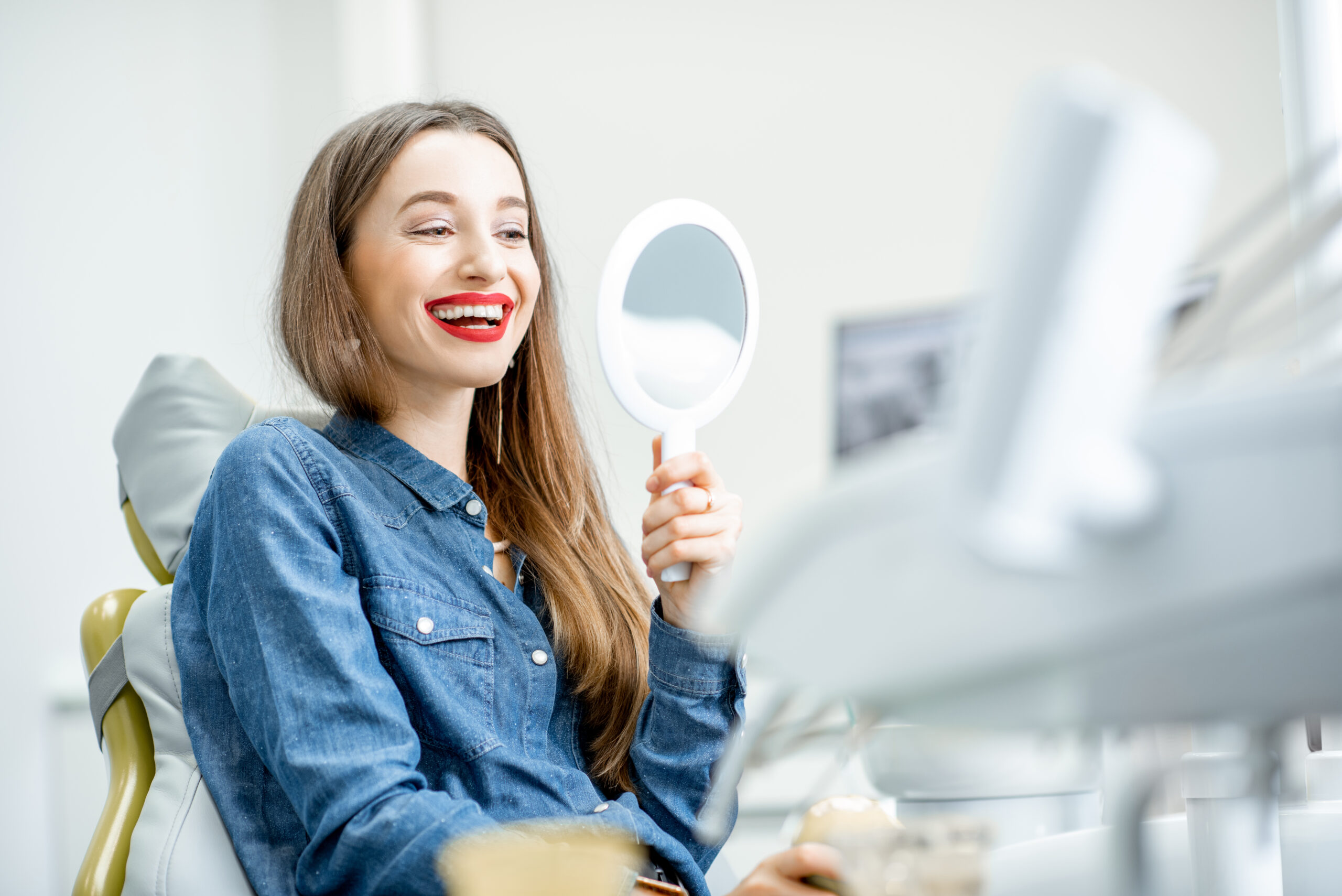 Portrait of a young beautiful woman looking on the mirror enjoying her beautiful smile in the dental office